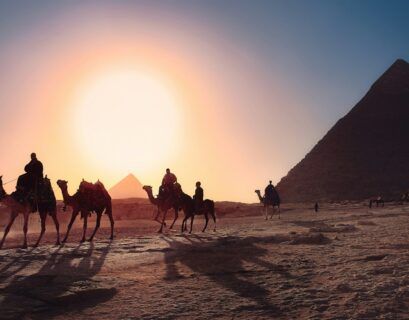 five persons riding camels walking on sand beside Pyramid of Egypt