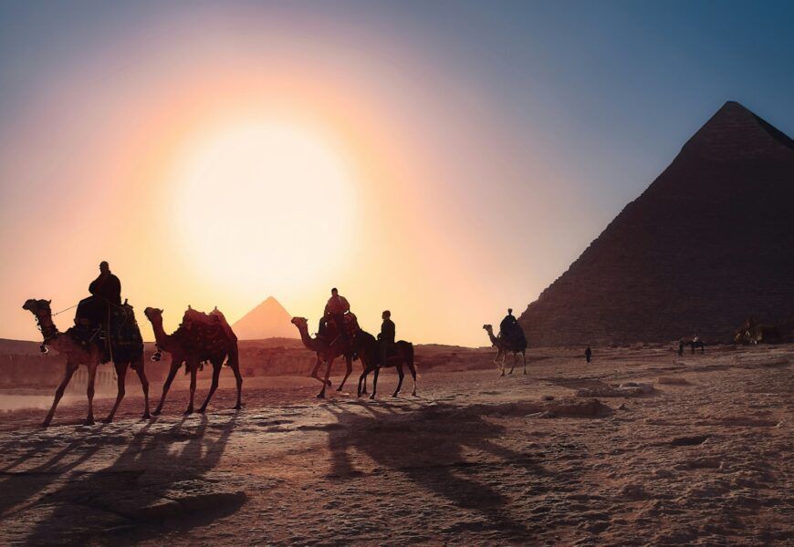 five persons riding camels walking on sand beside Pyramid of Egypt
